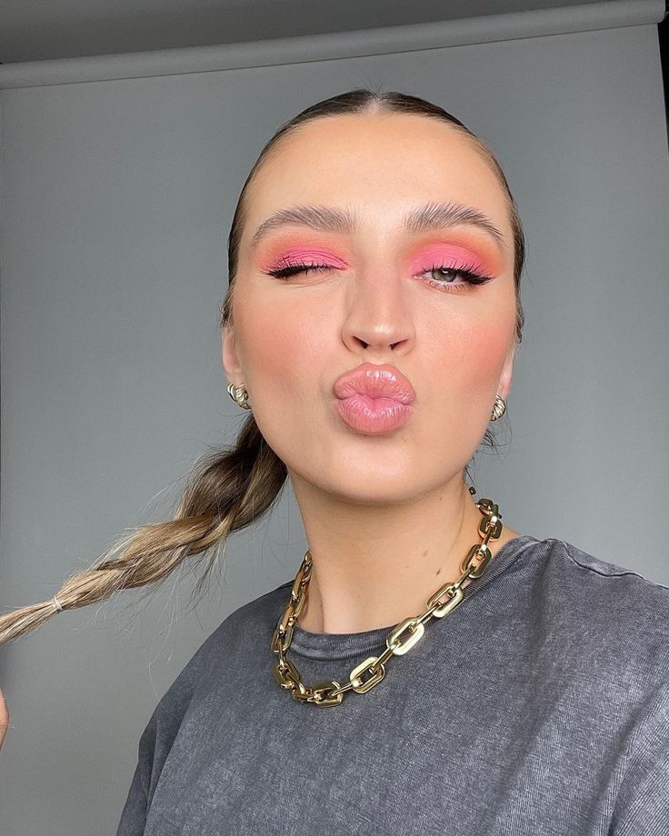 Mulher de pele clara, com camisa cinza, acessórios em dourado, cabelo preso em trança e maquiagem com tons de rosa pastel 