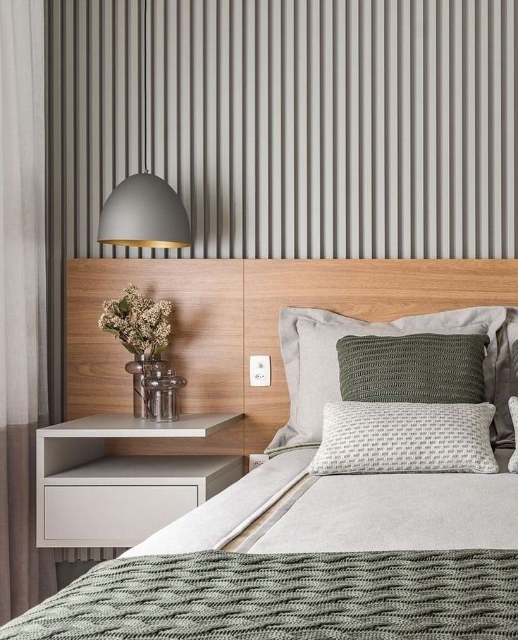 Quarto com cabeceira amadeirada e parede ripada cinza, com roupas de cama neutras e cinza