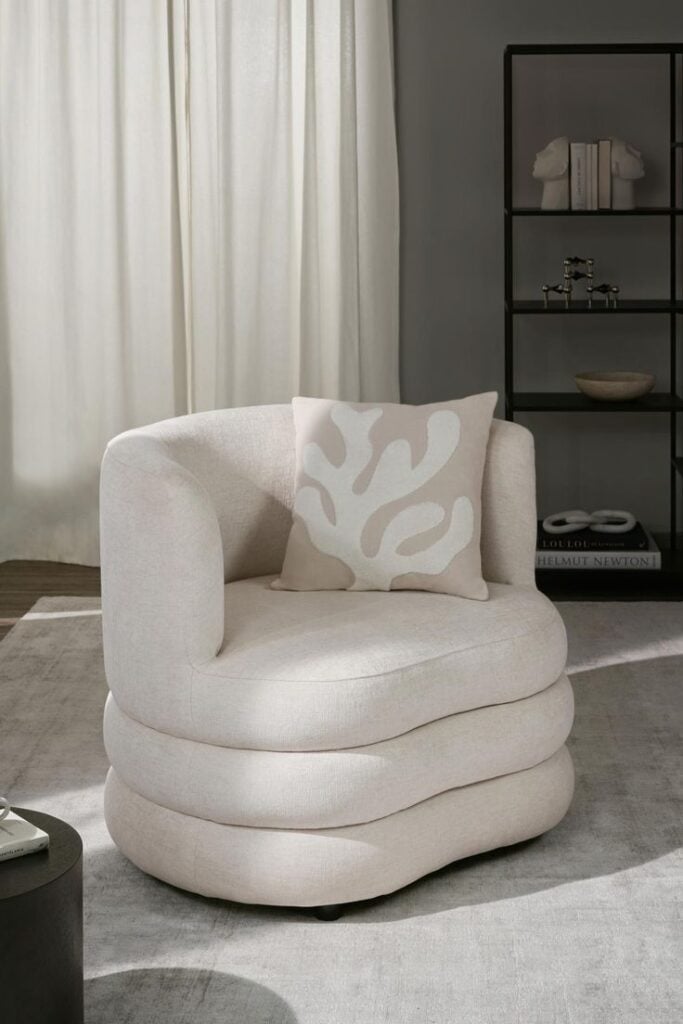 Poltrona de linhas orgânicas na cor off-white com uma almofada