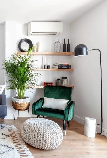 Ambiente com poltrona de veludo verde, luminária de piso e puff bege em crochê