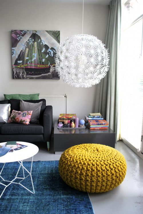 Sala com tapete azul, pendente e puff na cor mostarda