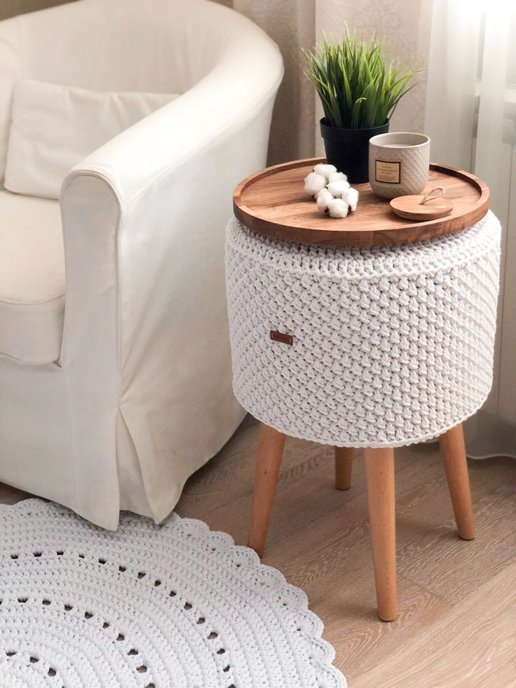 Puff bege de crochê com pés de madeira usado como mesa lateral na sala
