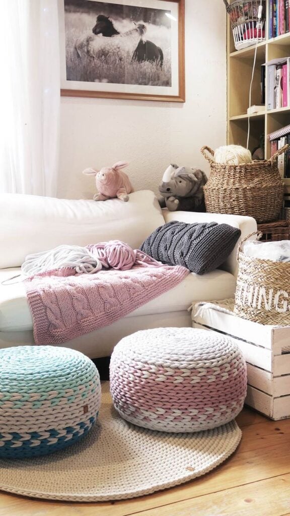 Sala com sofá claro e dois puff em tons de bege, rosa e azul