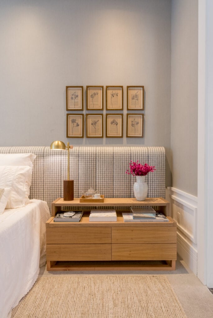 Quarto de casal com cama, cabeceira, quadros, flores e abajur
