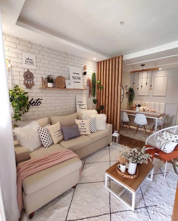 Sala com sofá em tom claro, parede de tijolinhos, almofadas e quadros