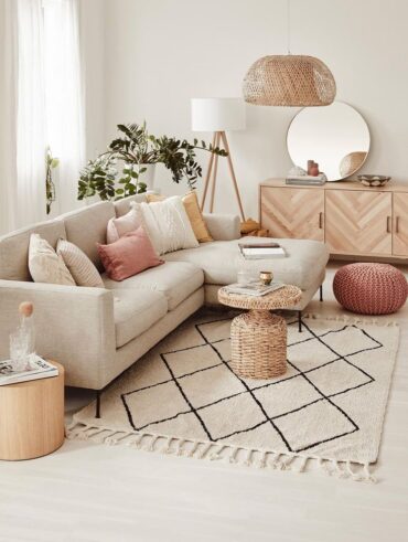 Sala pequena com sofá e elementos em cor neutra, puff e almofada rosé