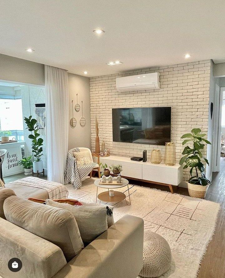 Sala com parede de tijolinhos, tapete grande na cor clara, puff e mesa de centro