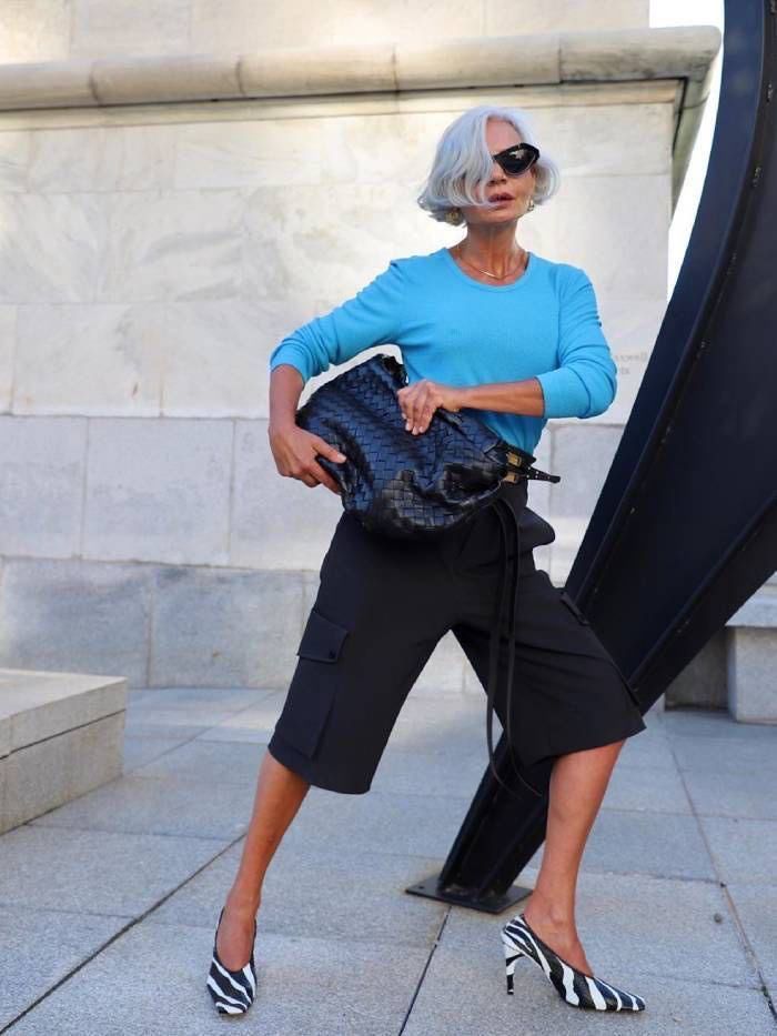 Grece Ghanem, com blusa azul, bermuda preta, bolsa preta e sapato com estampa de zebra