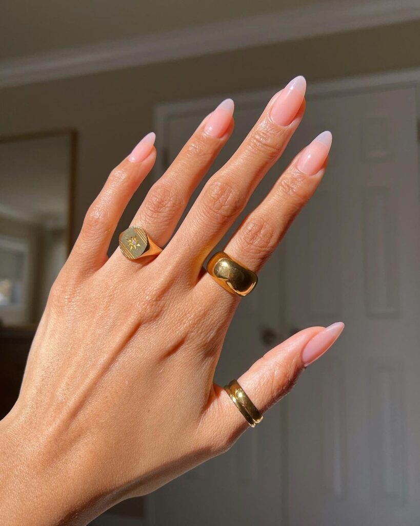 Mão de pele clara, com acessórios em dourado e unha amendoada estilo soap nails 