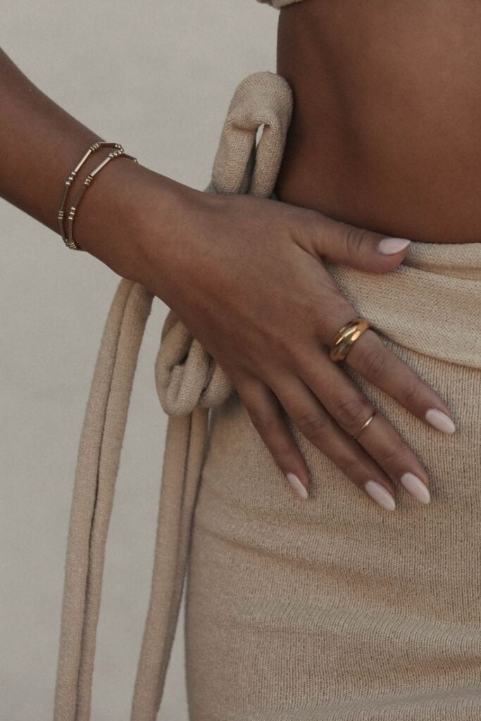 Mão de pele preta-clara, com acessórios em prata e dourado e unha amendoada branca
