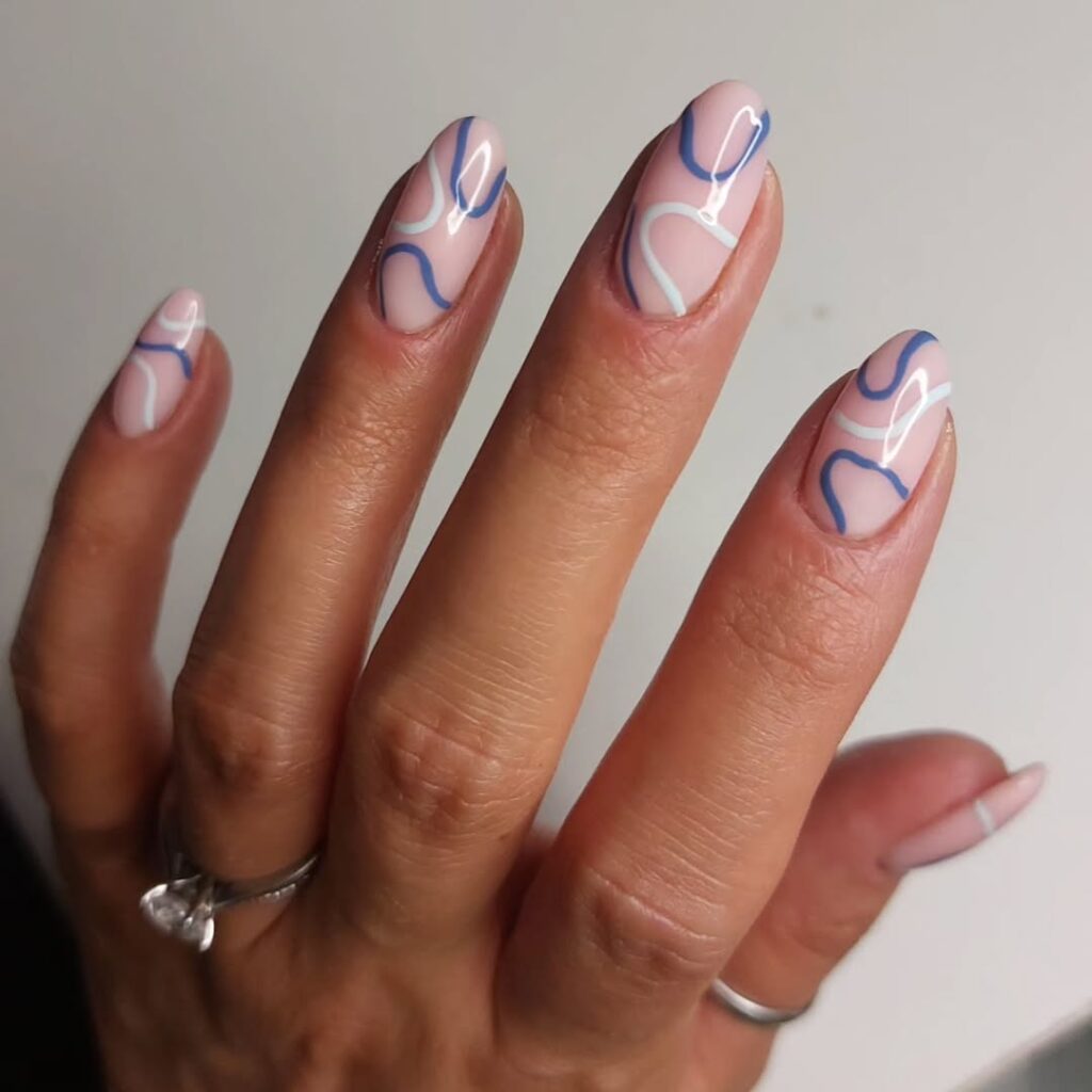 Mão de pele clara, com anéis em prata e unha amendoada nude com linhas fluidas em azul