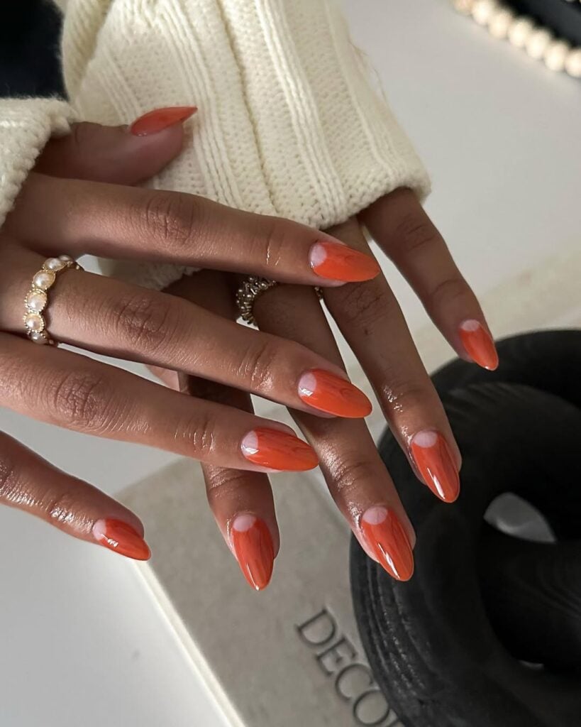 Mão de pele negra, com unha amendoada, com esmalte laranja e técnica de nail art cut out