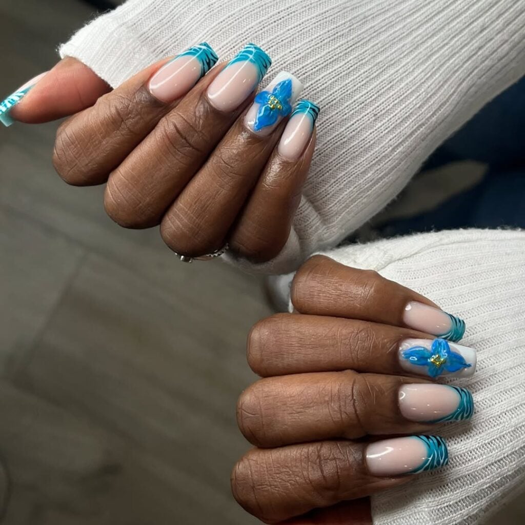 Mãos de pele preta, com anéis e unha bailarina com francesinha e detalhes em azul