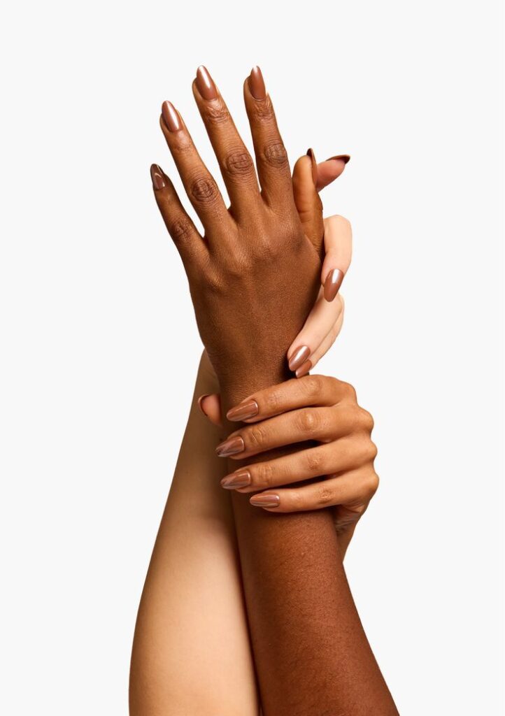 Mãos de pele branca e negra, com unha longa e amendoada e esmalte marrom opaco