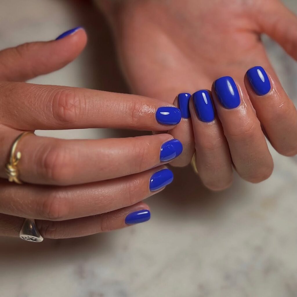 Mãos de pele clara, com acessórios em dourado e prata e unha quadrada e curta azul royal 