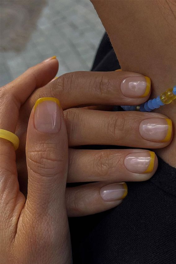 Mãos de pele clara, com unha curta com francesinha amarelo-mostarda