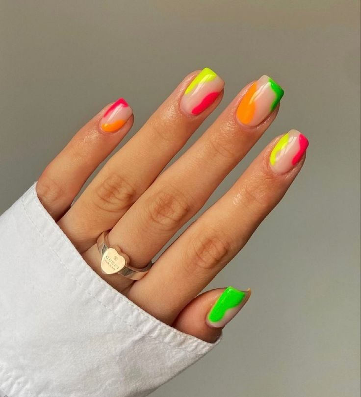 Mão de pele clara, com anel em dourado e unha curta e quadrada nude com decorações em neon