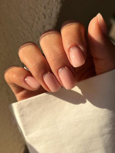 Mão de pele clara, com unha squoval nude com francesinha invertida de glitter