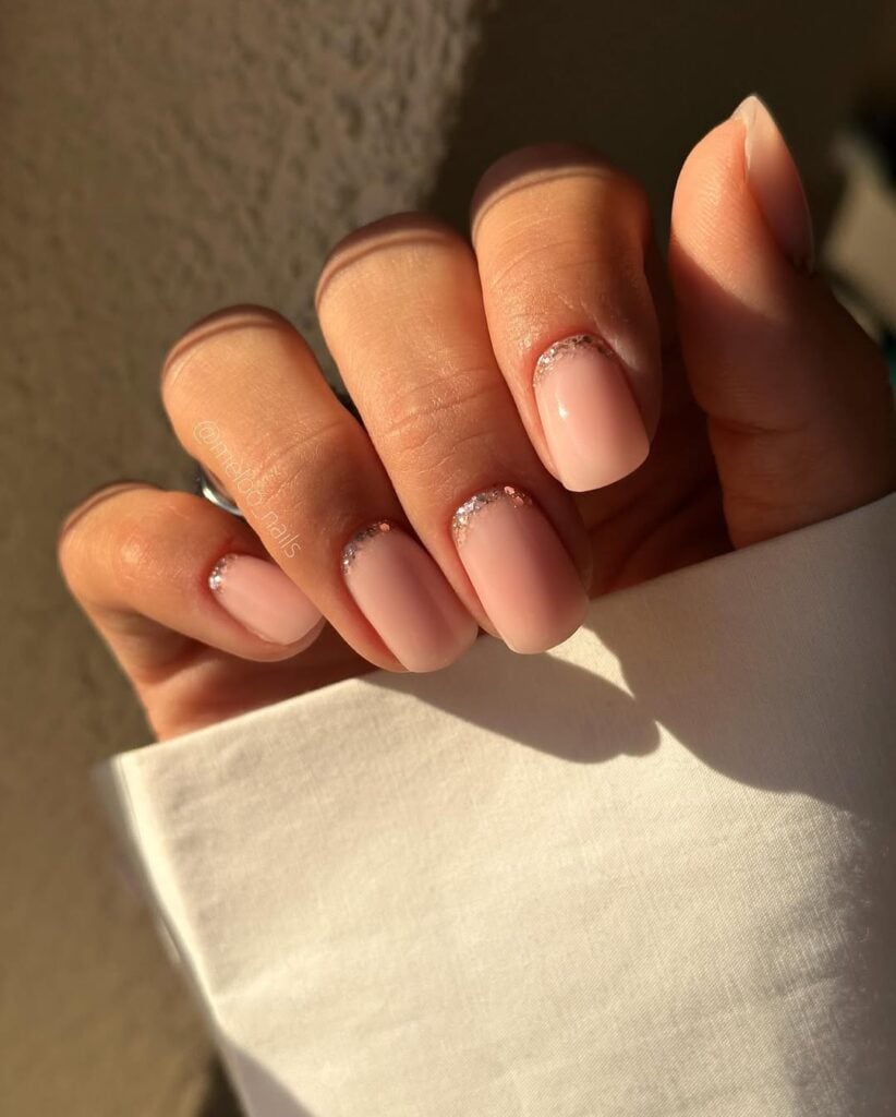 Mão de pele clara, com unha squoval nude com francesinha invertida de glitter