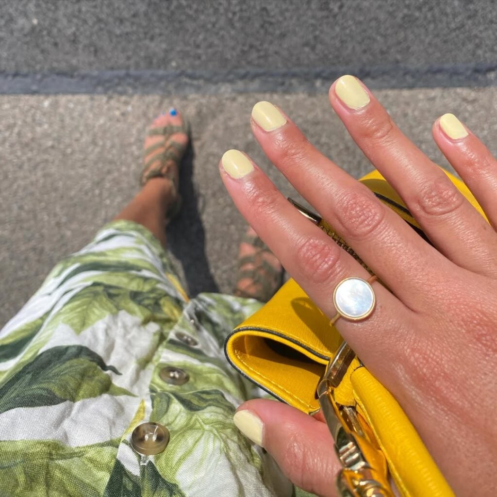 Mão de pele clara, com anel em dourado e unha curtinha amarelo-manteiga