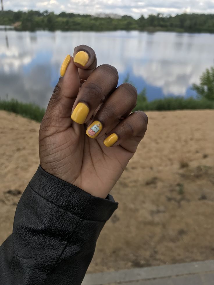 Mão de pele preta, com unha quadrada amarelo-mostarda com adesivo