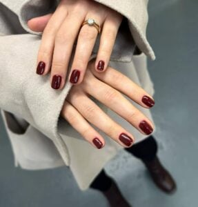 Mãos de pele clara, com anel dourado e unha curta black cherry