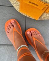 Pés de pele clara, com chinelo de amarração laranja e unha decorada laranja