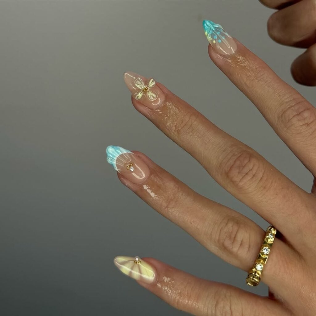 Mão de pele clara, com anel em dourado com unha nude com decoração inspirada no mar