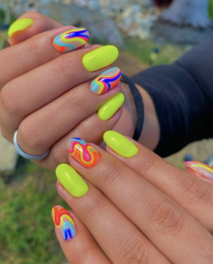 Mãos de pele clara, com anel colorido e unha amendoada neon com ondulações 