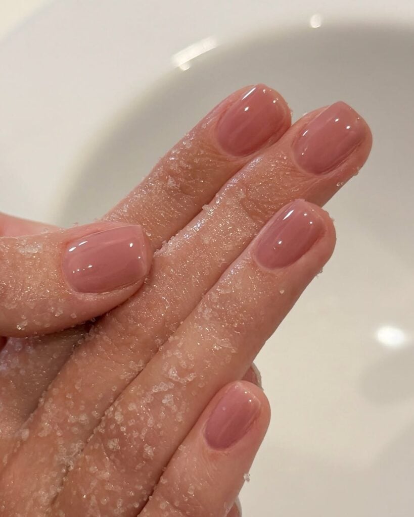 Mão de pele clara, com unha curta e squoval nude com fundo rosa