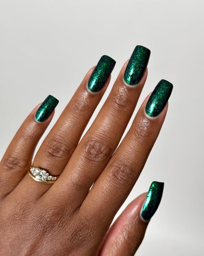 Mão de pele preta, com acessórios em dourado e unha quadrada verde-escuro com brilho