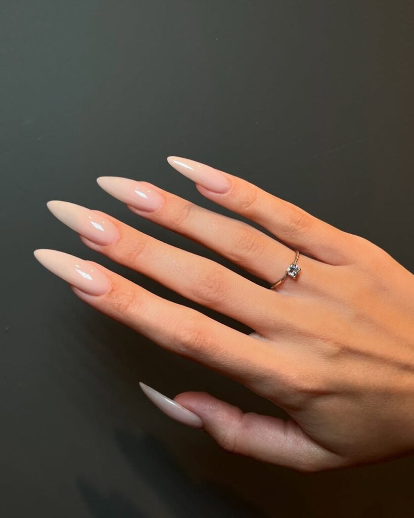 Mão de pele clara, com anel em dourado e unha stiletto comprida nude