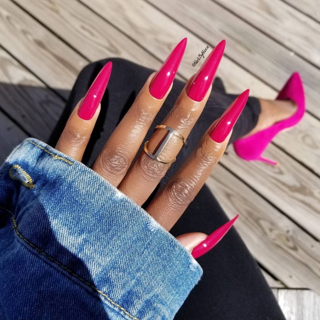 Mão de pele preta, com acessório em dourado e unha longa stiletto rosa-escuro