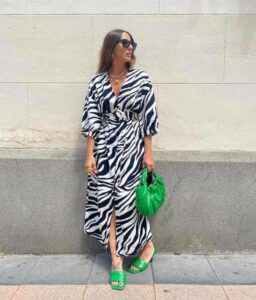 Mulher magra e de pele clara, com vestido zebrado e calçado e bolsa verde