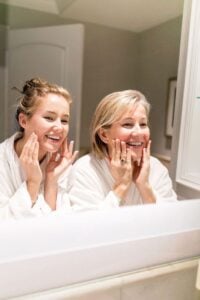 Duas mulheres de pele clara, uma mais velha que a outra, se olhando no espelho