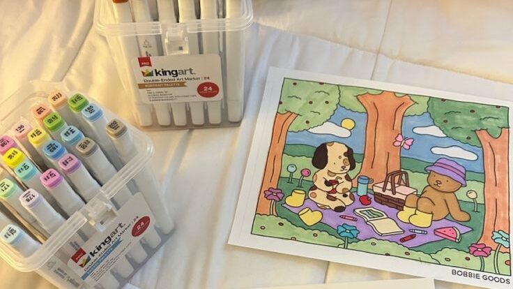 livro de colorir Bobbie Goods com desenhos de ursinhos e caixa com diversas canetinhas coloridas.