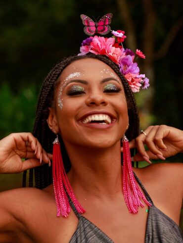 Mulher jovem de pele negra com tiara de flores rosas e roxas e brinco rosa comprido