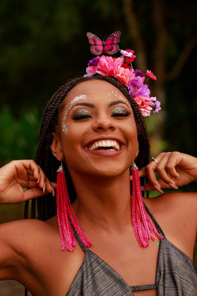 Mulher jovem de pele negra com tiara de flores rosas e roxas e brinco rosa comprido
