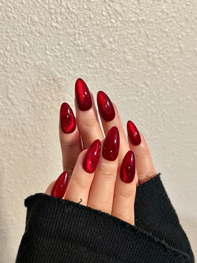 Mão de pele branca, com unha longa amendoada com esmalte vermelho, com nail art cat eye nails