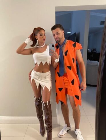 Mulher magra e de pele clara, com fantasia da Wilma Flintstone. E home de pele clara com fantasia do Fred Flintstone