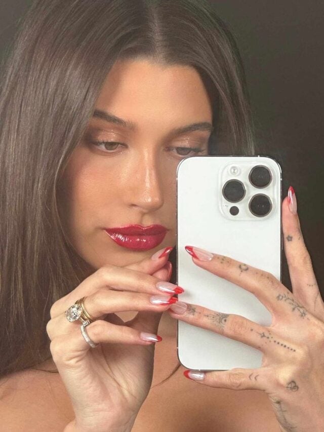 Hailey Bieber, com acessórios em dourado e unha com francesinha vermelha