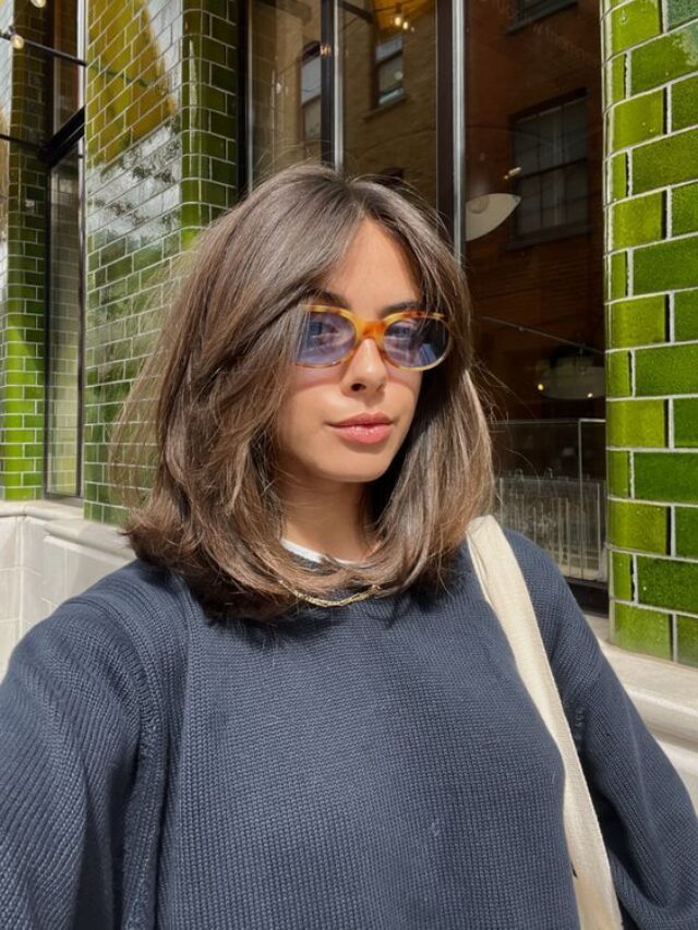 Mulher de pele clara, com suéter escuro, cabelo escuro com corte gatinho e óculos laranja