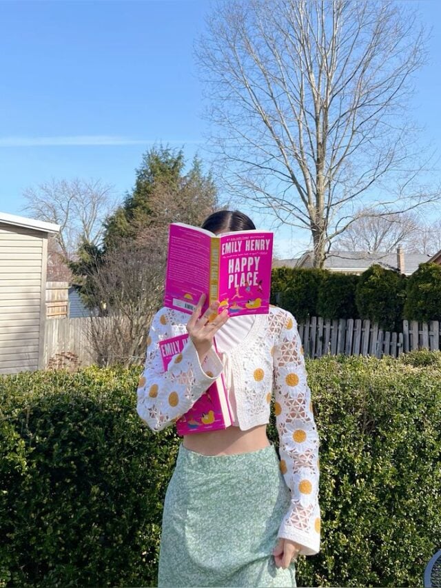 Mulher de pele clara, com roupa estampada, segurando o livro Lugar Feliz