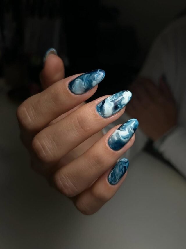 Mão de pele branca, com unha longa e amendoada, com esmalte azul e branco na nail art ocean nails