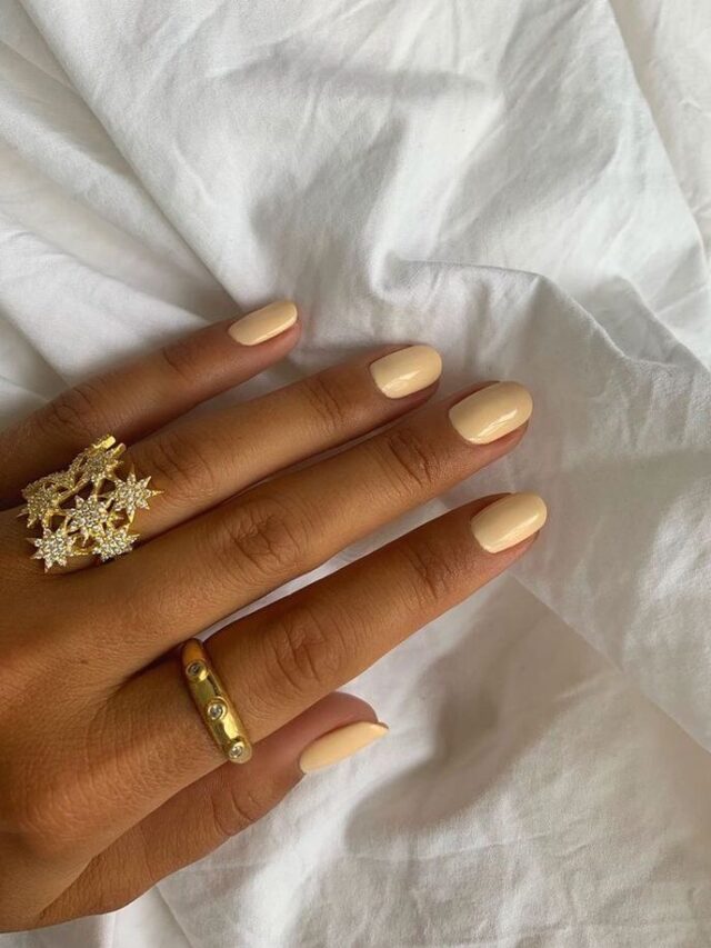 Mão de pele clara, com anéis em dourado e unha amendoada amarelo-claro