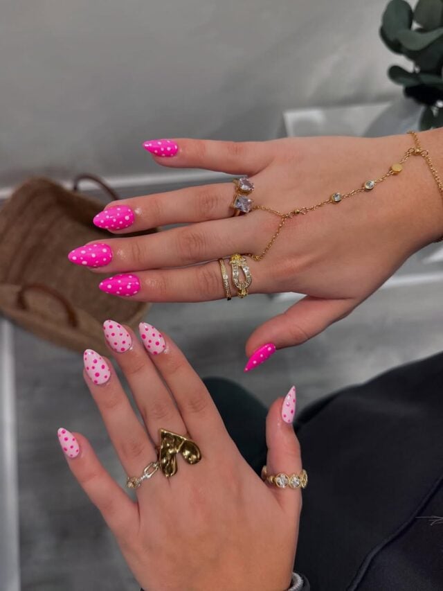 Mãos de pele clara, com acessórios em dourado e unha amendoada rosa com bolinhas rosa claro