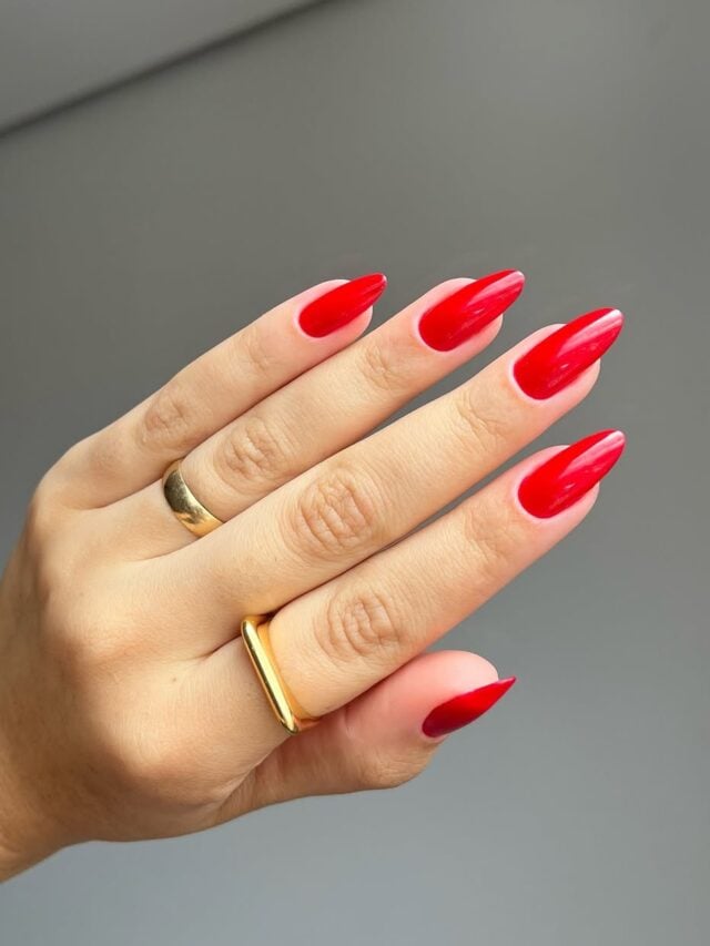 Mão de pele clara, com anéis em dourado e unha amendoada com esmalte vermelho Merengue da Dailus
