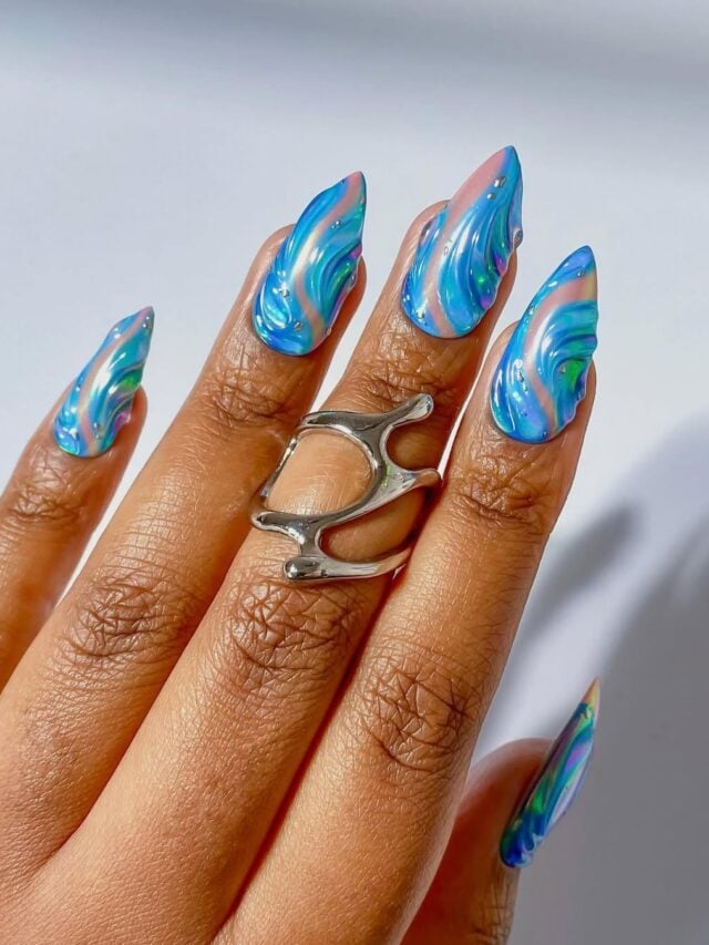 Mão de pele preta, com anel em prata e unha stiletto nude com detalhes em azul e com alto relevo
