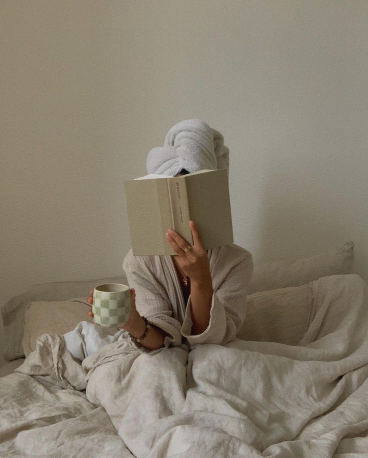 Mulher em cima de uma cama com um livro na frente do rosto