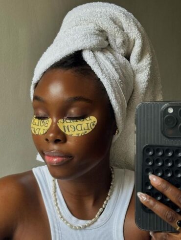 Mulher jovem de pele escura com toalha de banho na cabeça e máscara para os olhos.
